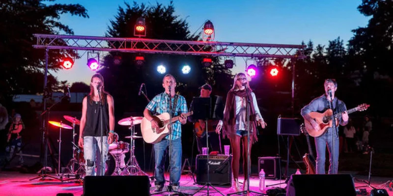Musicians play instruments and sing on a lit outdoor stage at Domaine des Ormes