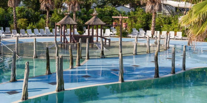 Gazebo on a wooden deck in a large swimming pool surrounded by lounge chairs and palm trees at Oyam