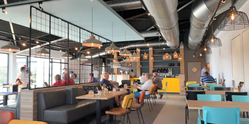 People are dining and socially interacting with others at tables in a brightly lit, modern café at Kompas Nieuwpoort