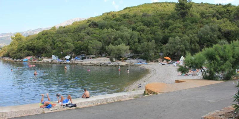 People relax and swim by a pebble beach, surrounded by greenery and hills at Aminess Port 9