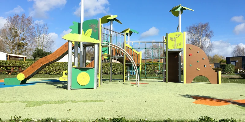 Playground structure with slides and climbing areas, in an open, grassy area with trees and blue sky at Mont Saint Michel