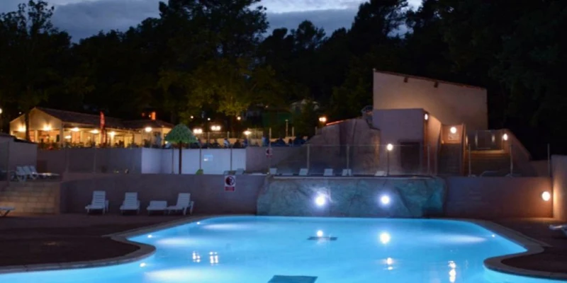Illuminated swimming pool at dusk with surrounding lounge chairs, near a lit building amidst trees at Lou Cantaire