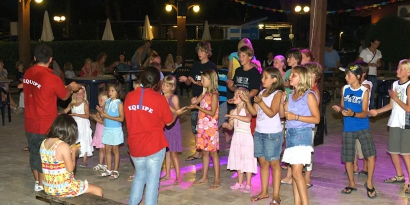 Children stand together and dance under colorful lights, guided by instructors in red shirts at River