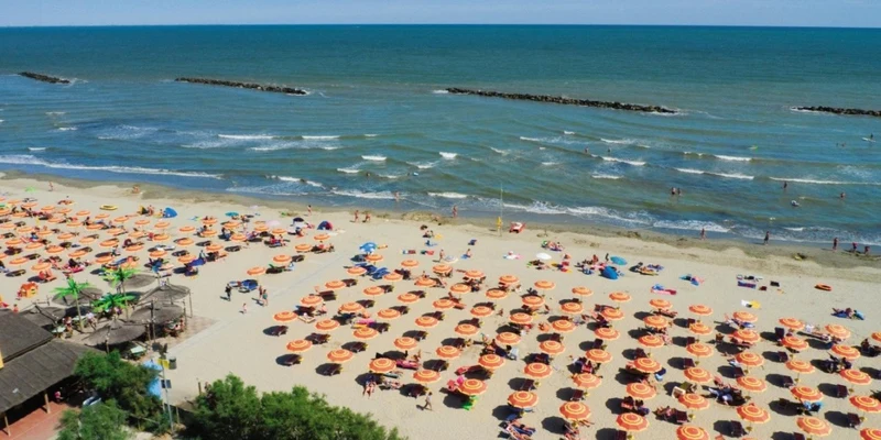 Orange umbrellas and sunbathers are on a sandy beach near the shoreline, with gentle waves in the background at Spiaggia e Mare