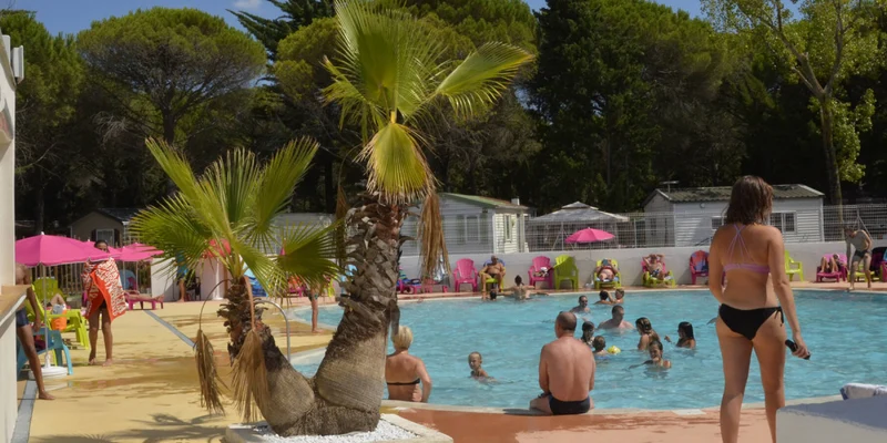 People swimming and relaxing around a pool surrounded by palm trees and colorful chairs at Maïana Resort