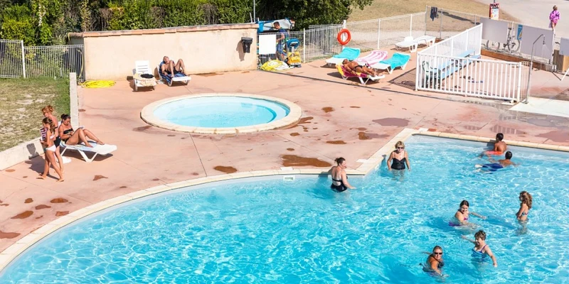 People enjoying a swim and sunbathing by a large pool and hot tub, surrounded by greenery and lounge chairs at Marvilla Parks Le Val de Durance
