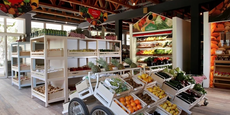 Wooden crates filled with assorted fruits and vegetables on display racks inside a market, surrounded by wooden shelves and signage at Amadria Park Camping Sibenik 