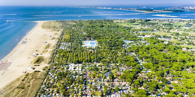 Aerial view of beach and forest campsite with numerous tents and facilities near the ocean at Marina di Venezia