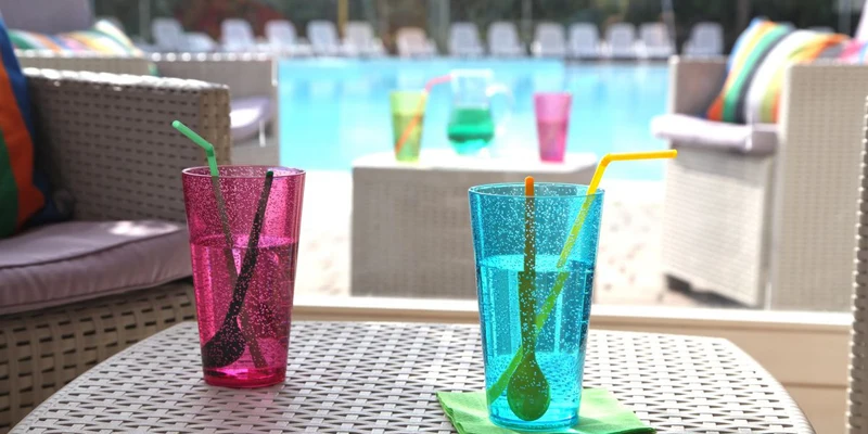 Two colorful drinks with straws on a wicker table, overlooking a pool area with lounge chairs at Europa Silvella