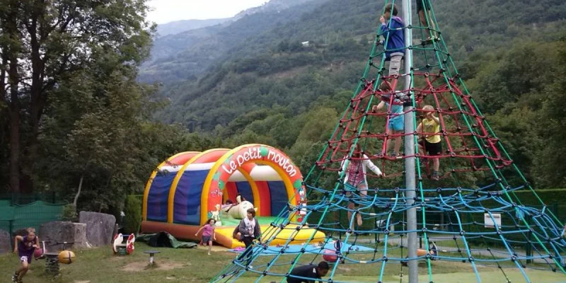 Children climb on a tall rope pyramid and play near a colorful inflatable bouncer in a scenic mountainous area at Airotel Pyrénées