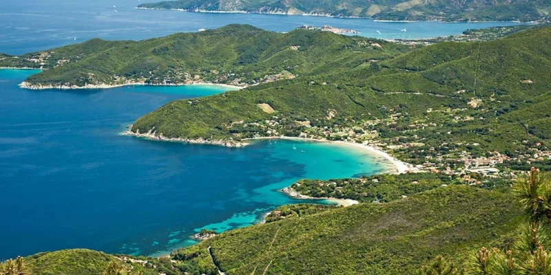 Aerial view of coastal hills and turquoise bays, with adjacent villages and distant mountains at Rosselba le Palme