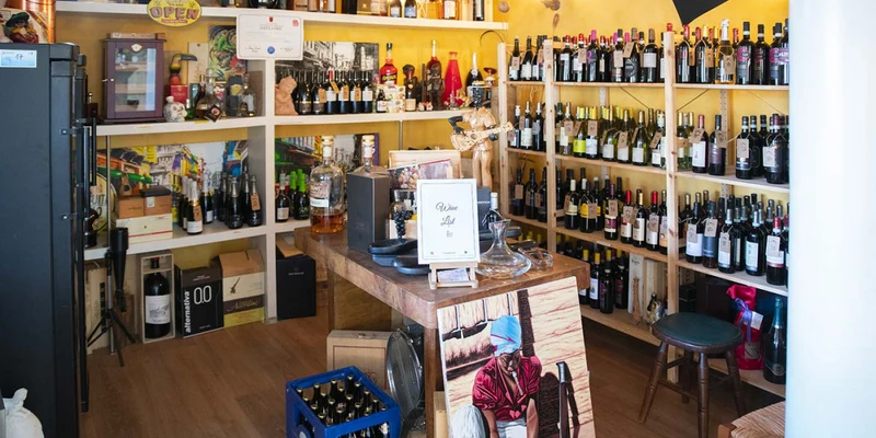Wine bottles displayed on wooden shelves in a cozy room with a small table holding various beverages and decor at Eden