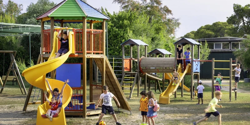 Children playing on a colorful playground structure with slides and climbing frames, surrounded by trees at Riva di Ugento