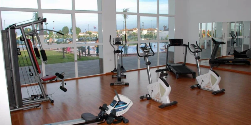 Exercise equipment stands idle in a gym room with large windows overlooking an outdoor area at Lo Monte