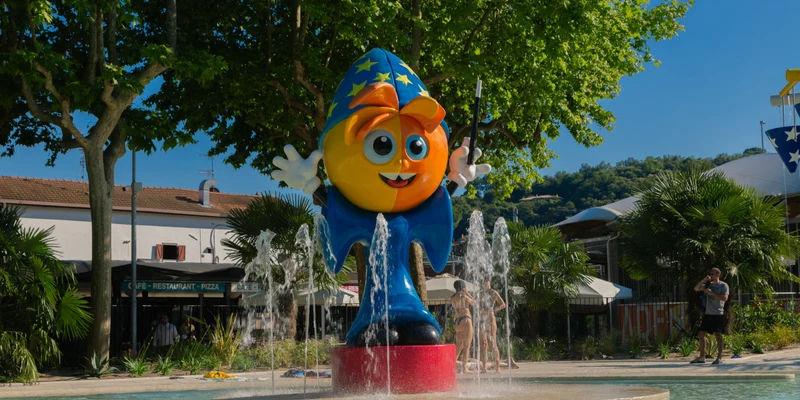 Colorful wizard statue in a fountain, surrounded by trees and buildings at Village Lago Maggiore