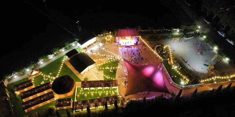Aerial view of a lit-up outdoor event with tents, a stage, and people gathered at Free Time
