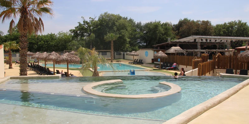 Swimming pools with palm trees and sun loungers by thatched umbrellas, adjacent to a cafeteria and outdoor seating at Paradis le Pearl