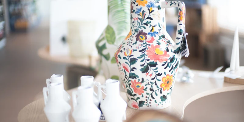 Colorful ceramic pitcher with floral patterns stands on a table surrounded by small white vases, within a shop at Roompot Callantsoog