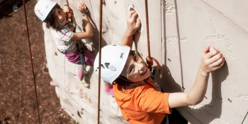 Children climbing an artificial rock wall, secured by harnesses at Domaine des Ormes