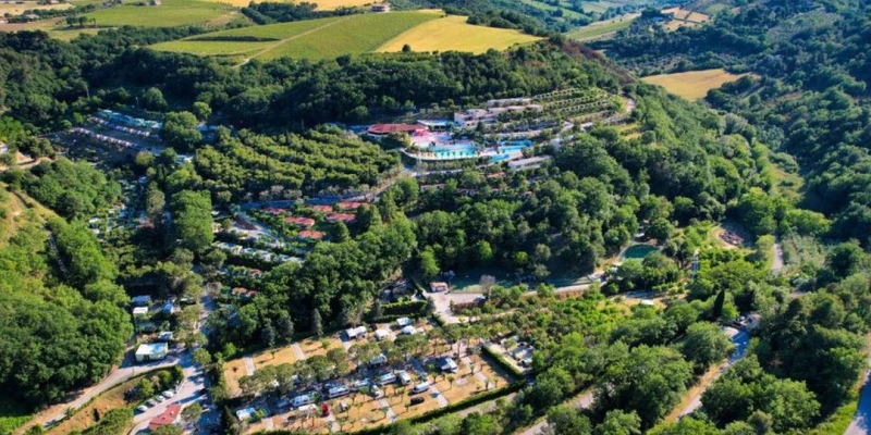 Aerial view of a lush, tree-covered campsite surrounded by rolling hills and open fields at Camping Village Mirage
