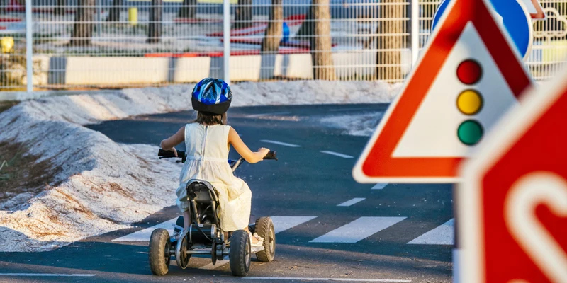 A child on a tricycle rides past traffic signs on a paved path near a fence at Zaton Holiday Resort
