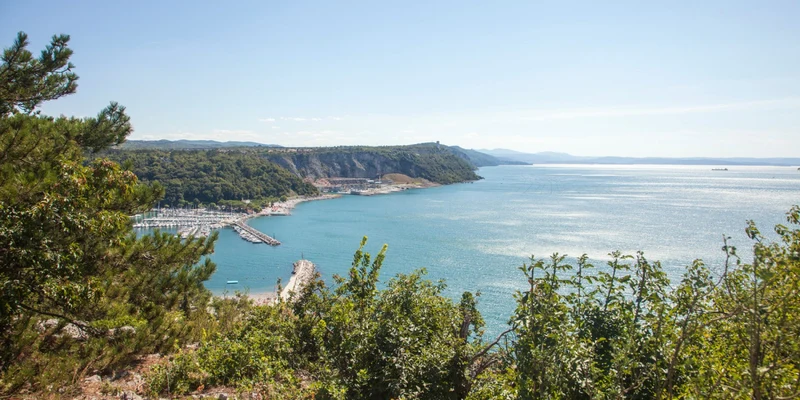 Ocean bay lined with trees; distant hilly shoreline and docked boats on a clear day at Camping Mare Pineta