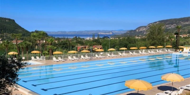 A large swimming pool with yellow umbrellas and lounge chairs overlooking greenery and distant mountains at Poiano