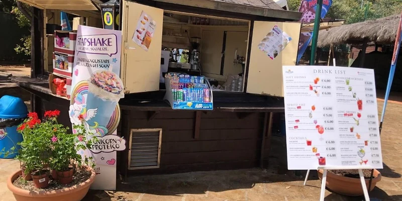 A wooden snack stand serves drinks, surrounded by colorful plants and promotional signs at Stella del Mare