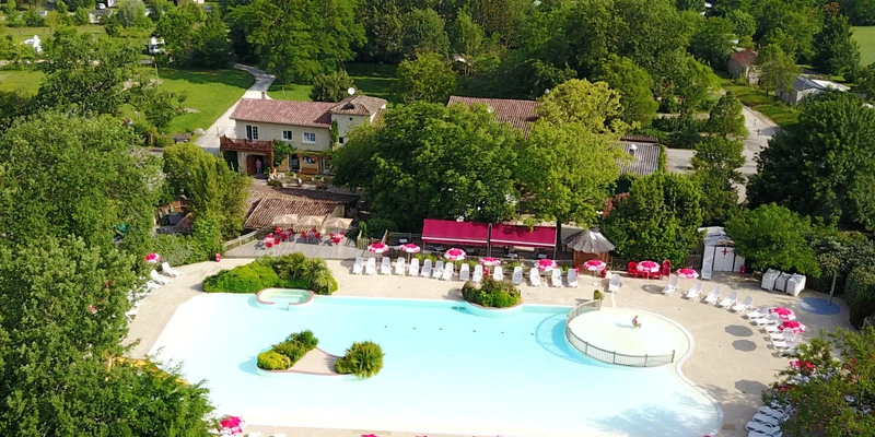Swimming pool surrounded by pink umbrellas and lounge chairs, positioned near buildings and trees, in a lush green landscape at Le Camp de Florence