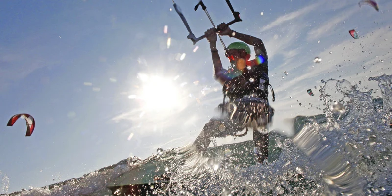 Kitesurfer riding a wave, silhouetted against the sun, with water splashing around at Eurosurf