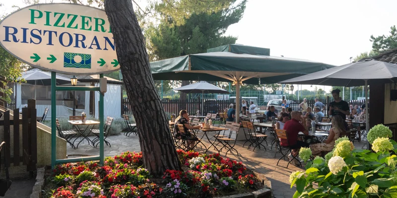 Outdoor dining tables filled with people eating and chatting, surrounded by colorful flowers and large umbrellas; at Punta Spin