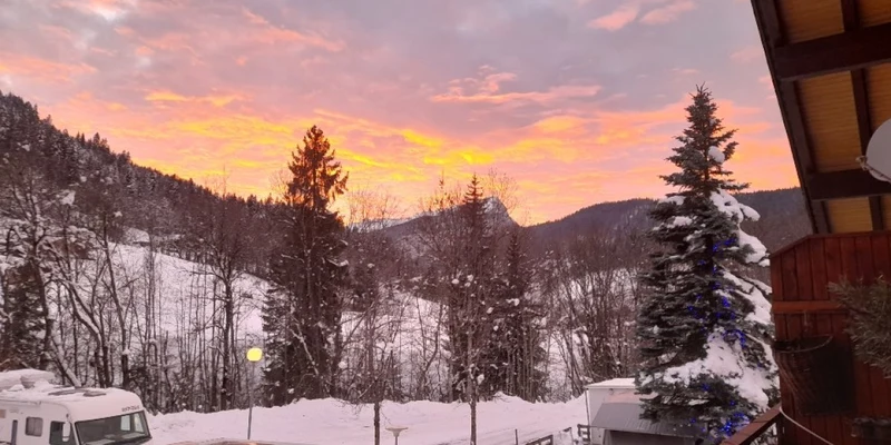Snow-covered RVs and trees at sunset against a mountain backdrop at Clos du Pin