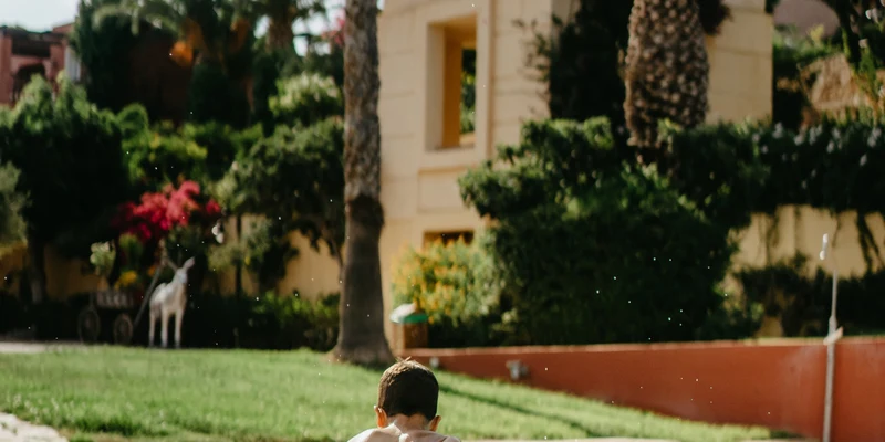 Boy jumping into a swimming pool in front of a tall building and palm trees at Candia Park Village