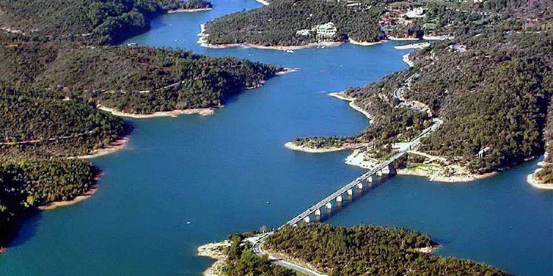 Bridge spans river with dense forested hills and scattered buildings at Les Lauriers Roses