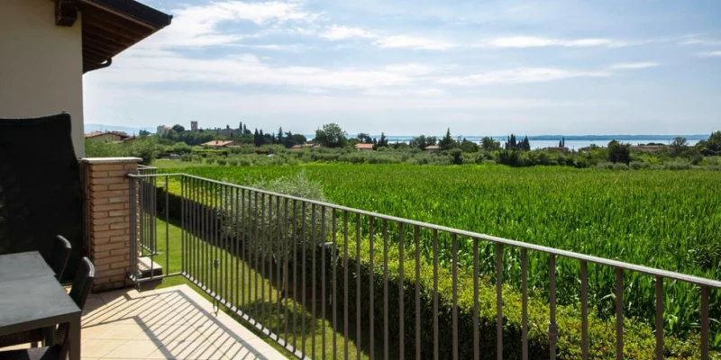 Balcony overlooking a lush green field with distant trees and a glimpse of a lake under a partly cloudy sky at Lake Garda Resort