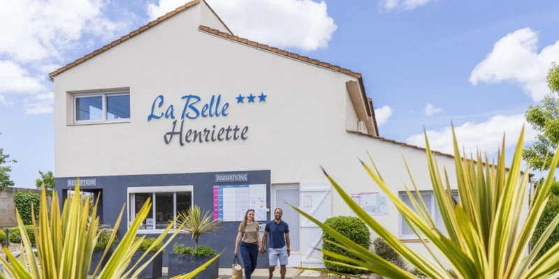 Two people walk away from a white building with signs at La Belle Henriette