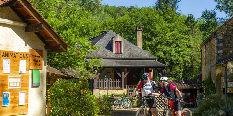 Cyclists pausing near a rustic building amidst greenery and other cabins at Aqua Viva