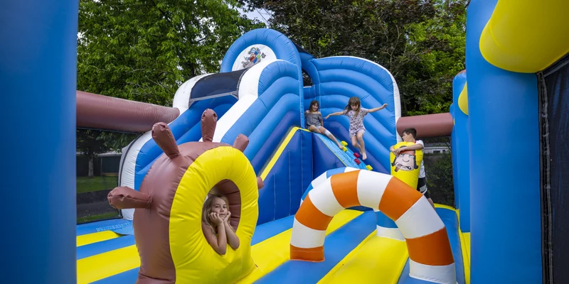 Children playing on a colorful inflatable obstacle course in a park, surrounded by trees at La Citadelle