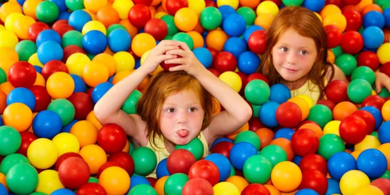 Two children playfully enjoying a colorful ball pit, surrounded by bright red, yellow, blue, and green balls at Duinrell