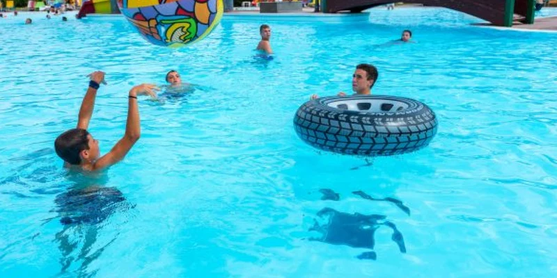 Children playing with colorful inflatables in a pool, surrounded by others swimming and a footbridge in the background at Residence Eden