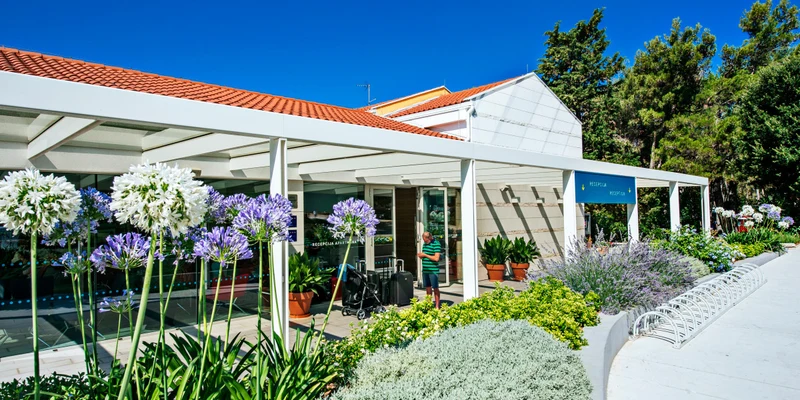 Building with flowers in front, surrounded by greenery under a clear blue sky at Zaton Holiday Resort