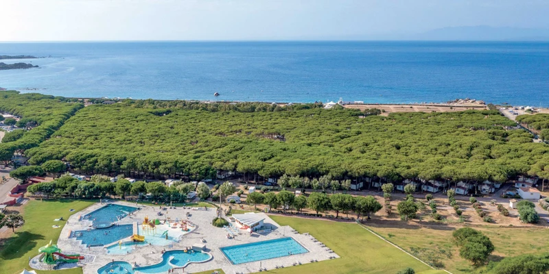 Swimming pools with slides and people relaxing, surrounded by green trees, next to the ocean at Baia Blu La Tortuga