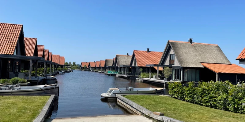 Row of cottages with red roofs line a narrow canal with small boats docked, surrounded by greenery at Waterstaete Ossenzijl