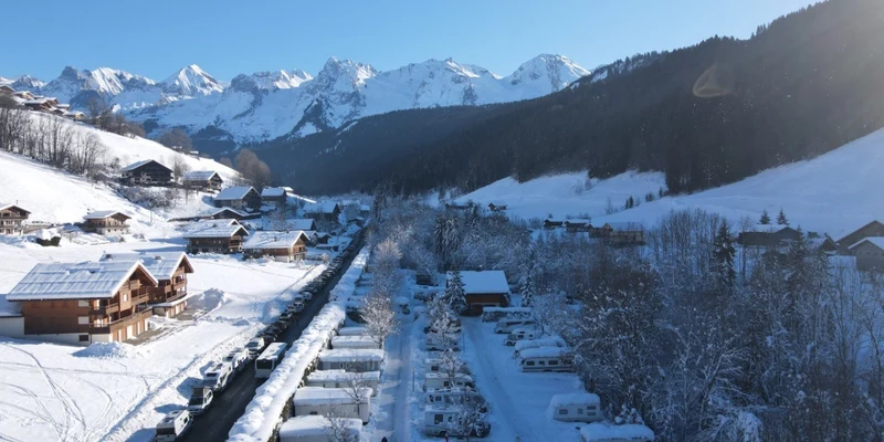 Several caravans parked in snowy campsite, surrounded by trees and mountains under a clear sky at Clos du Pin