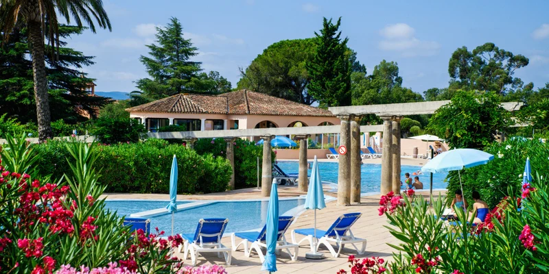 Swimming pool area with sun loungers and umbrellas surrounded by lush greenery and colorful flowers, near a building at Les Parcs de Grimaud
