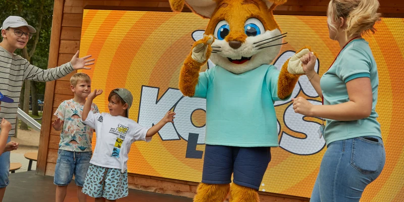 Costumed character dancing with children and adults on stage, with a brightly colored background at Kijkduinpark
