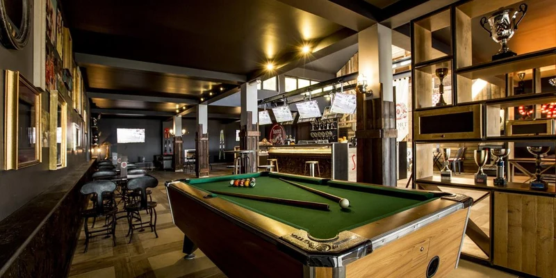 Pool table sitting in the center of a sports bar, surrounded by stools, pictures, and trophy shelves at Amadria Park Camping Trogir