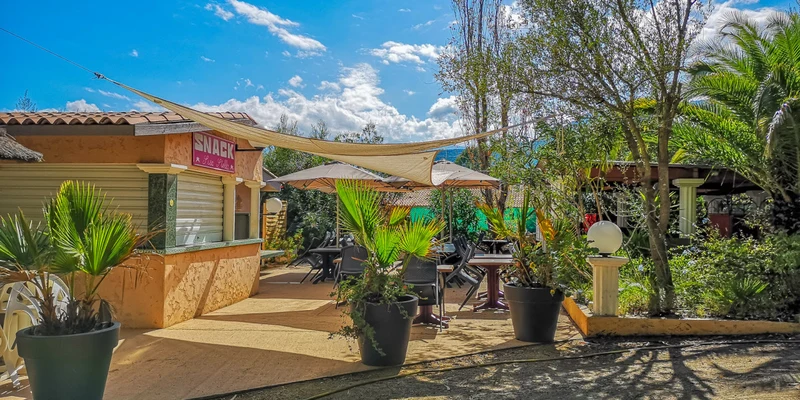 Snack bar with outdoor seating, shaded by canopies, surrounded by potted plants and trees at Bella Vista