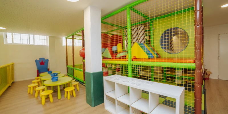 Children's indoor play area with colorful climbing structures and small tables and chairs, in a brightly lit room at Alannia Guardamar