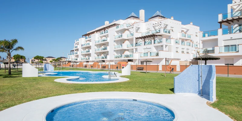 Circular pool with bubbling water, adjacent to a larger pool and modern white apartment buildings under a clear blue sky at Alméria Roquetas de Mar